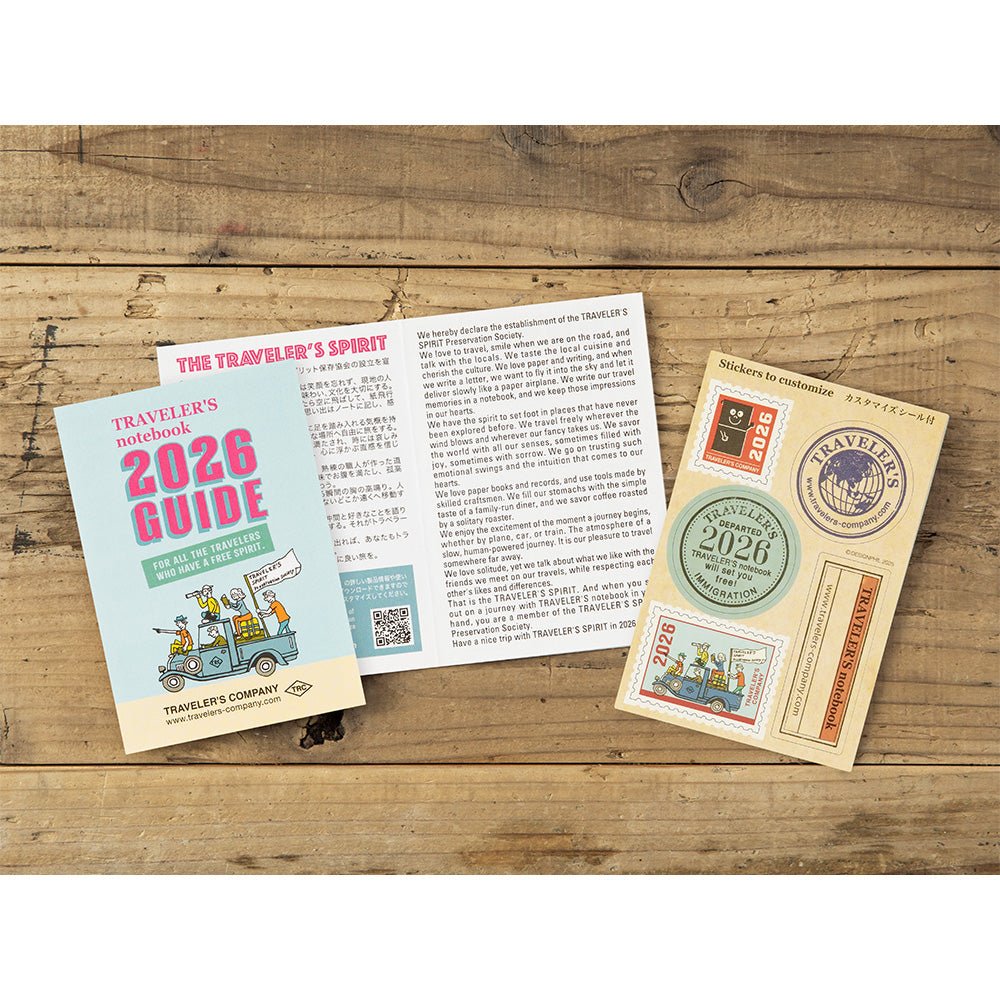 TRAVELER'S notebook passport size 2026 planner with horizontal week over two pages layout. Showing the opened TRAVELER'S notebook 2026 guide leaflet and the included sticker booklet