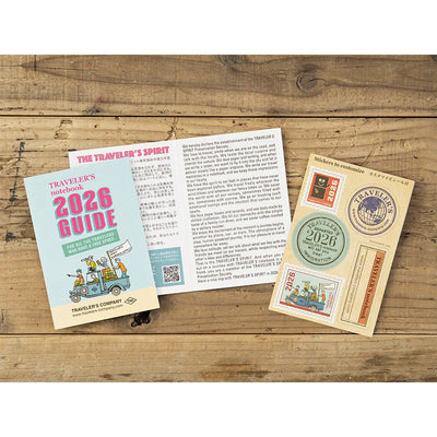 TRAVELER'S notebook passport size 2026 planner with horizontal week over two pages layout. Showing the opened TRAVELER'S notebook 2026 guide leaflet and the included sticker booklet