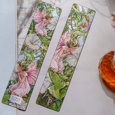 Two colorful Paperlanks Cicely Mary Barker fairy bookmarks on a book with a decorative bottle in the background.