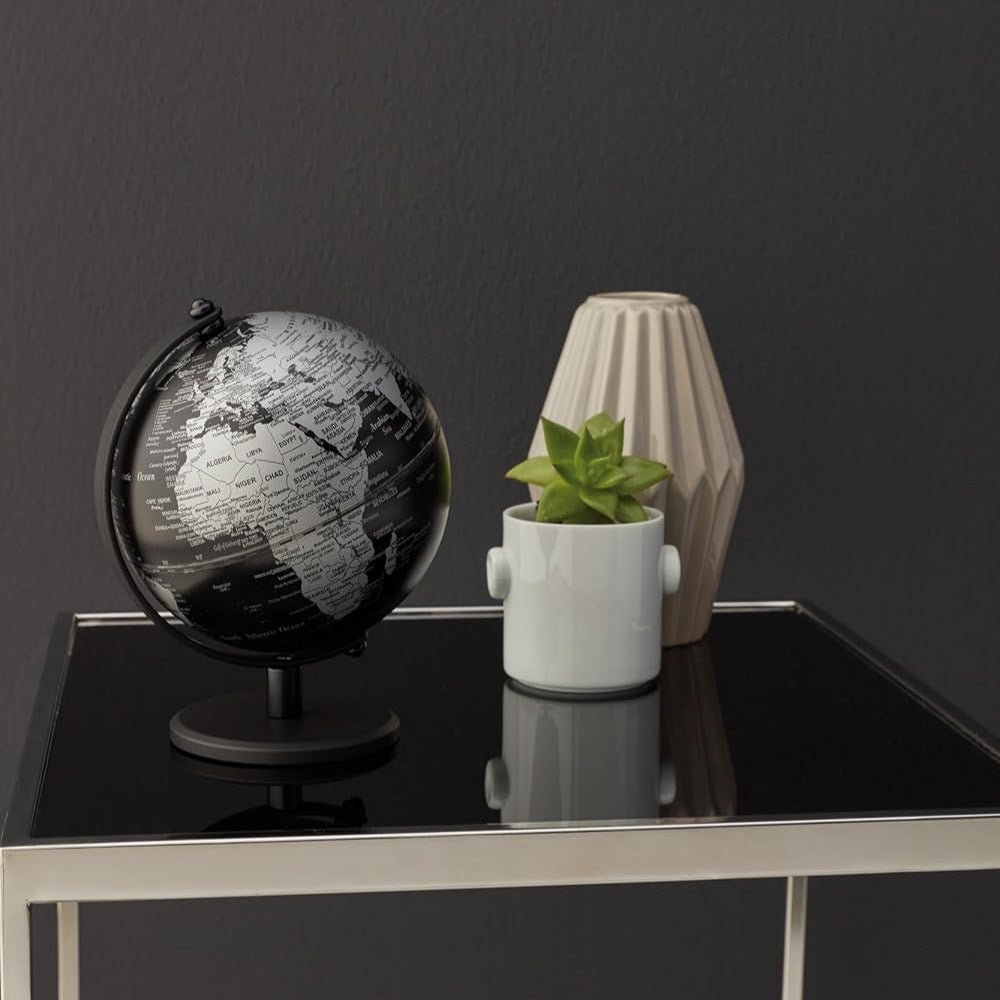 5 inch black and silver Troika globe, small plant, and decorative vase on a black surface against a dark gray wall.