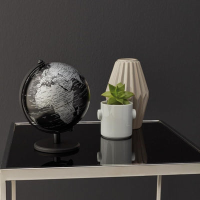 5 inch black and silver Troika globe, small plant, and decorative vase on a black surface against a dark gray wall.