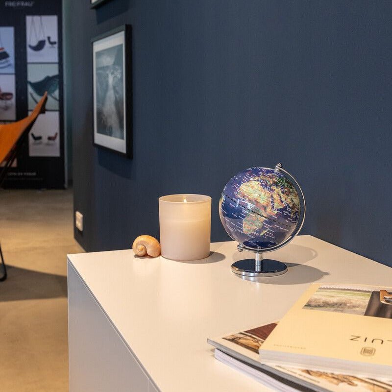 Small multi-color Troika globe on a white surface with a candle and books against a dark blue wall.